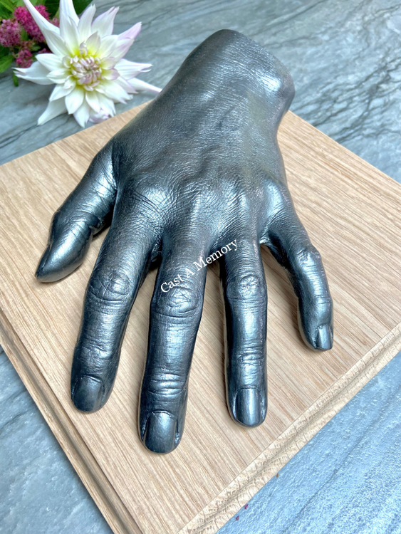 silver painted cast of a single hand on a wooden base