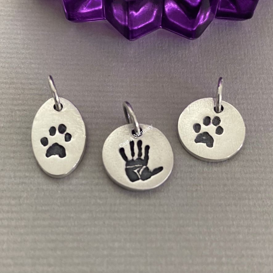 three tiny silver charms showing a paw print and hand print